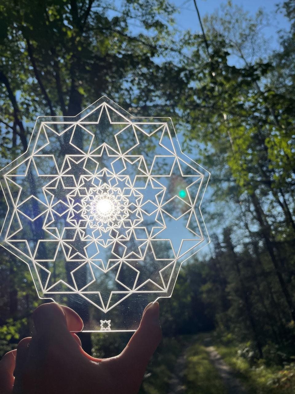 Hand-held acrylic recursive star aligned with sunlight in a forest